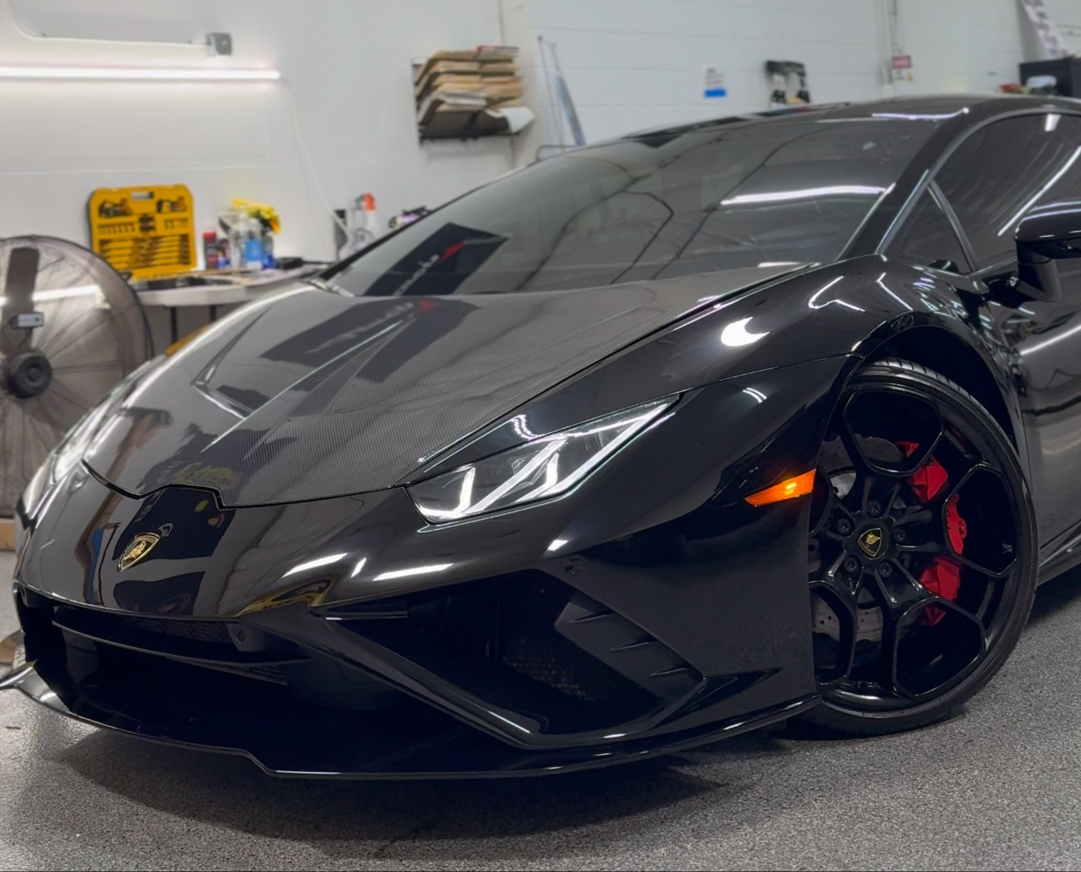 Black Lamborghini sports car in a garage with various brand flags on the wall.