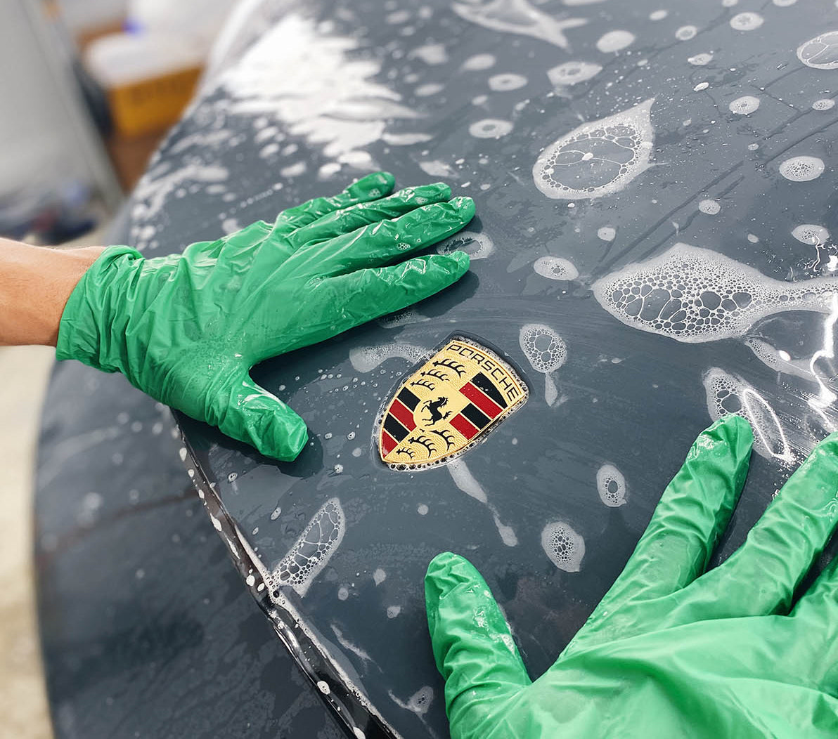 Paint protection expert wearing green gloves applying ppf on a Porsche at the studio in Tampa, Florida